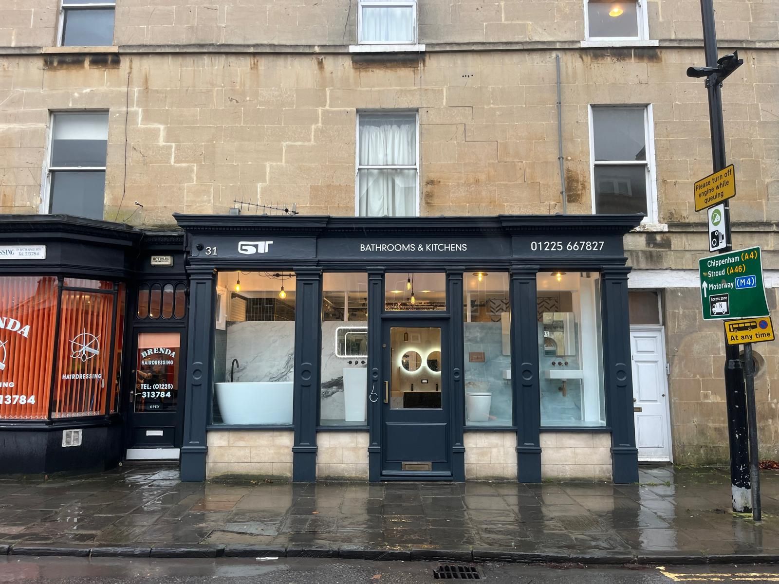 Exterior of a bathroom store with a dark facade, glass windows, and a display of bathroom fixtures.