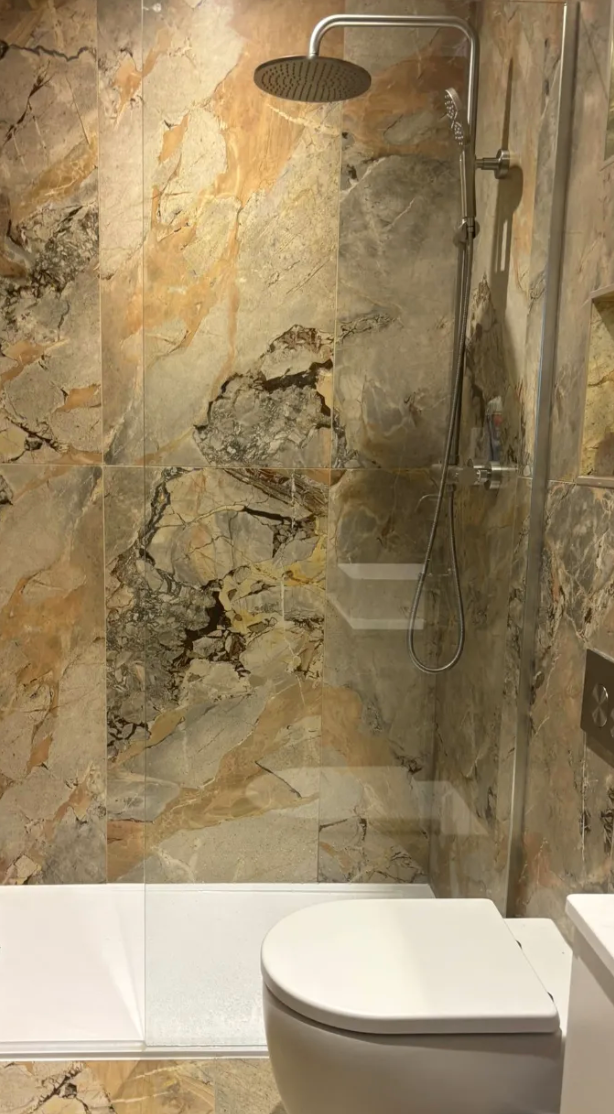 Bathroom with marble-patterned shower walls, showerhead, bathtub, and toilet.
