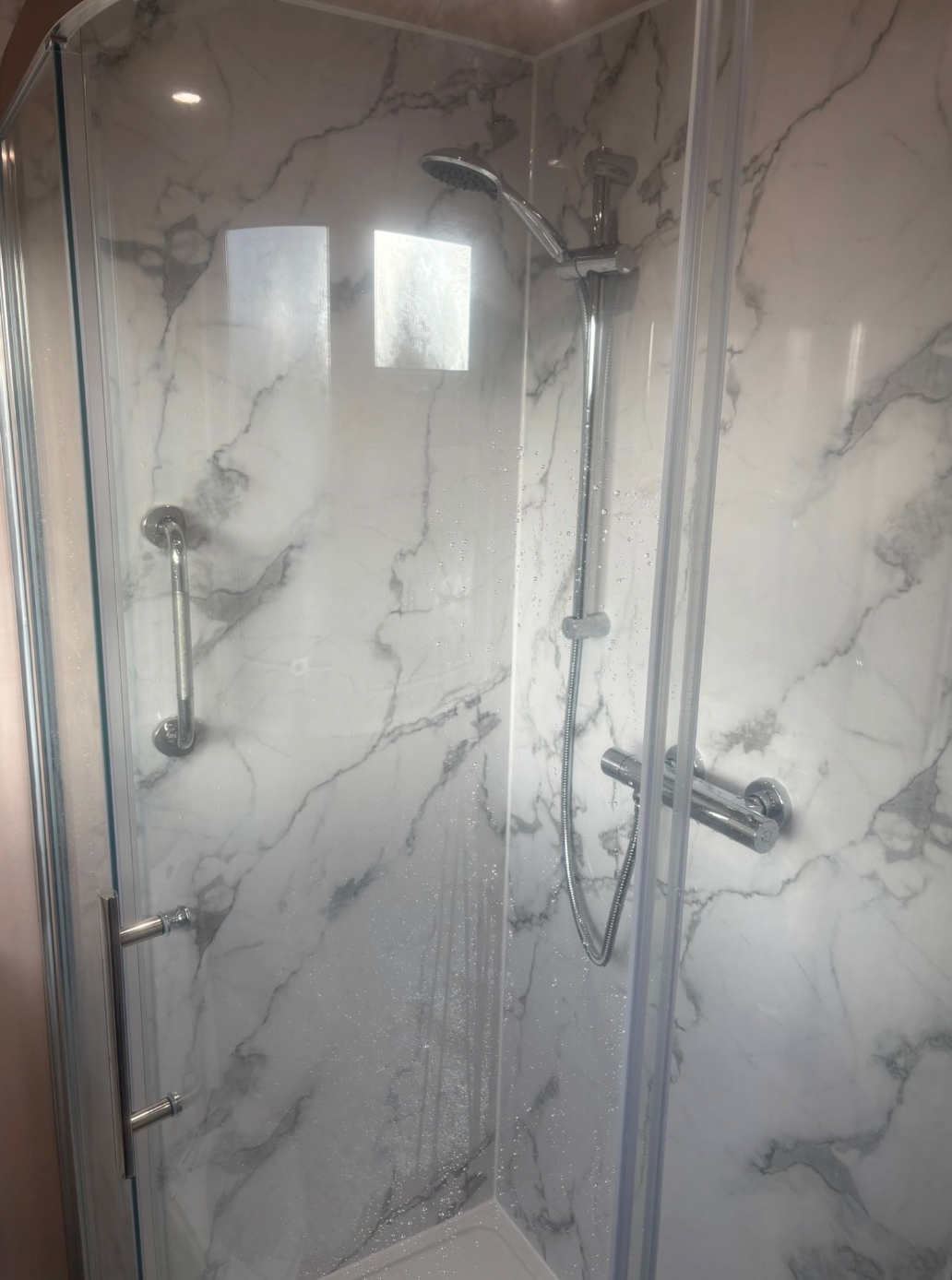 Shower with white marble-patterned walls and glass doors. Silver shower head and fixtures are visible.