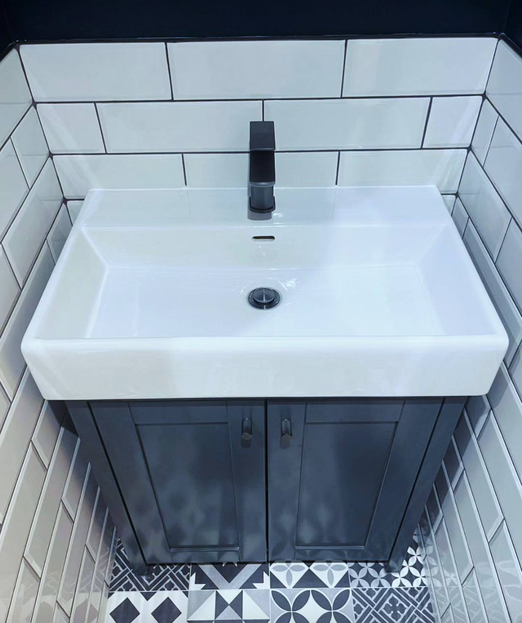 A bathroom sink with a black cabinet and white tiles.