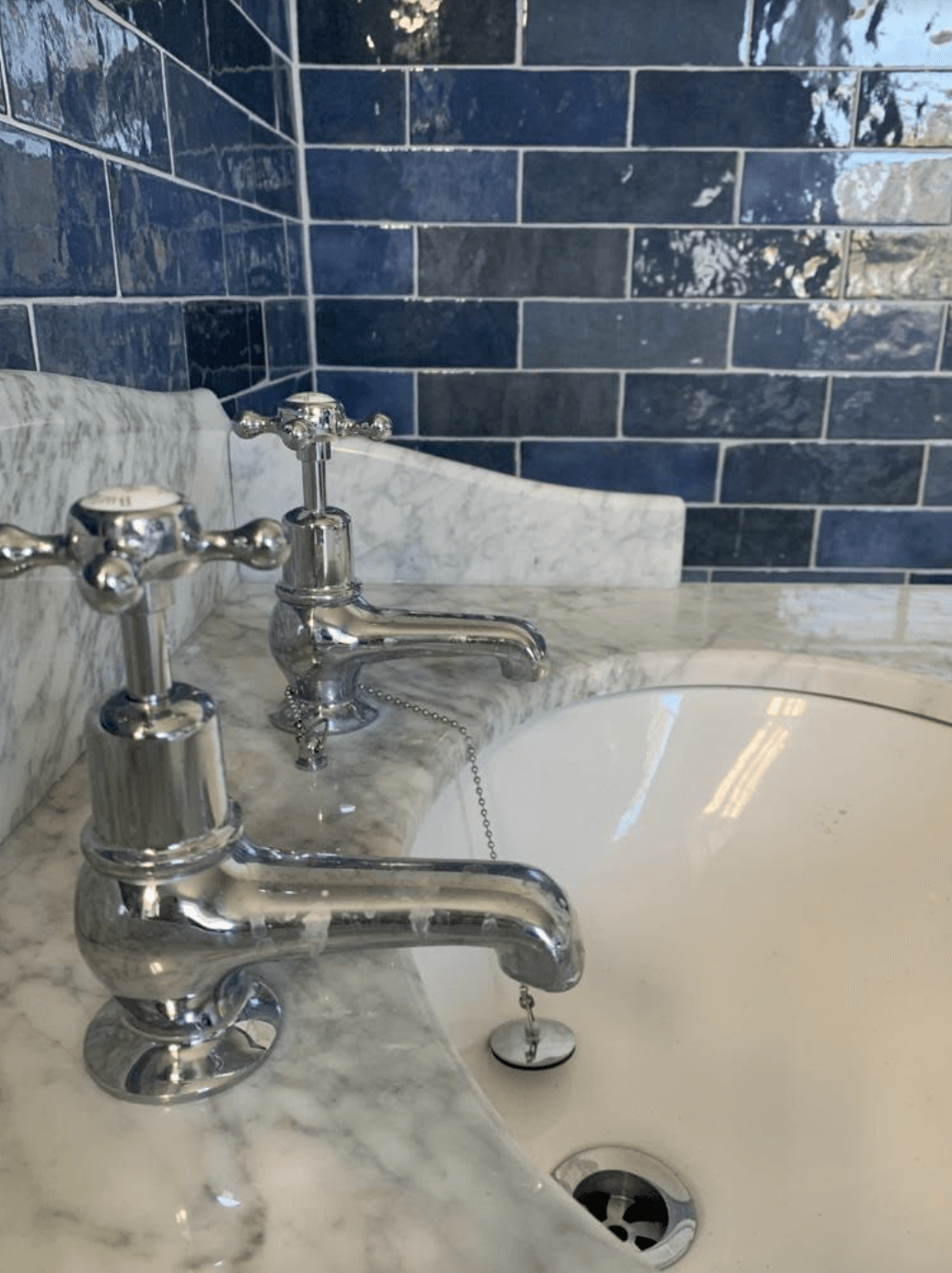A bathroom sink with two chrome faucets and blue tiles.