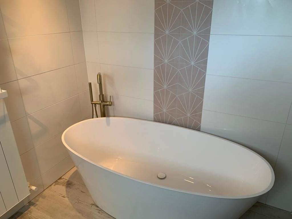 White oval bathtub in a modern bathroom with gold fixtures and geometric tile accents.