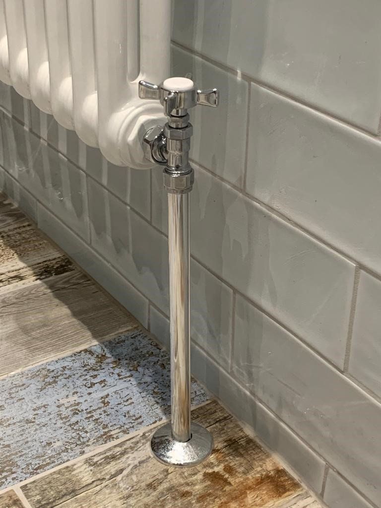 A close up of a radiator on a tiled floor next to a brick wall.