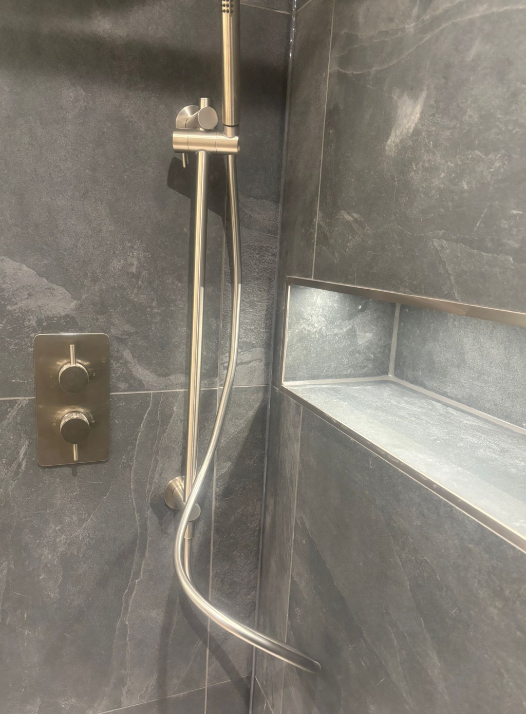 Shower with dark gray tile walls, built-in shelf, and silver showerhead and controls.