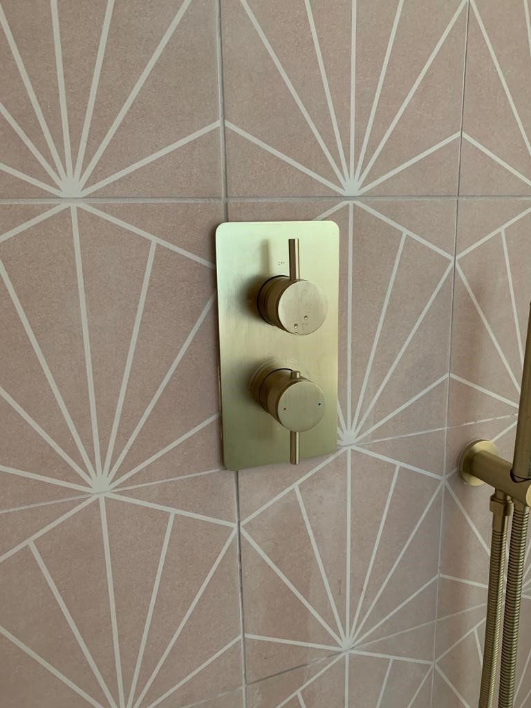 A close up of a brass shower head on a pink tiled wall.