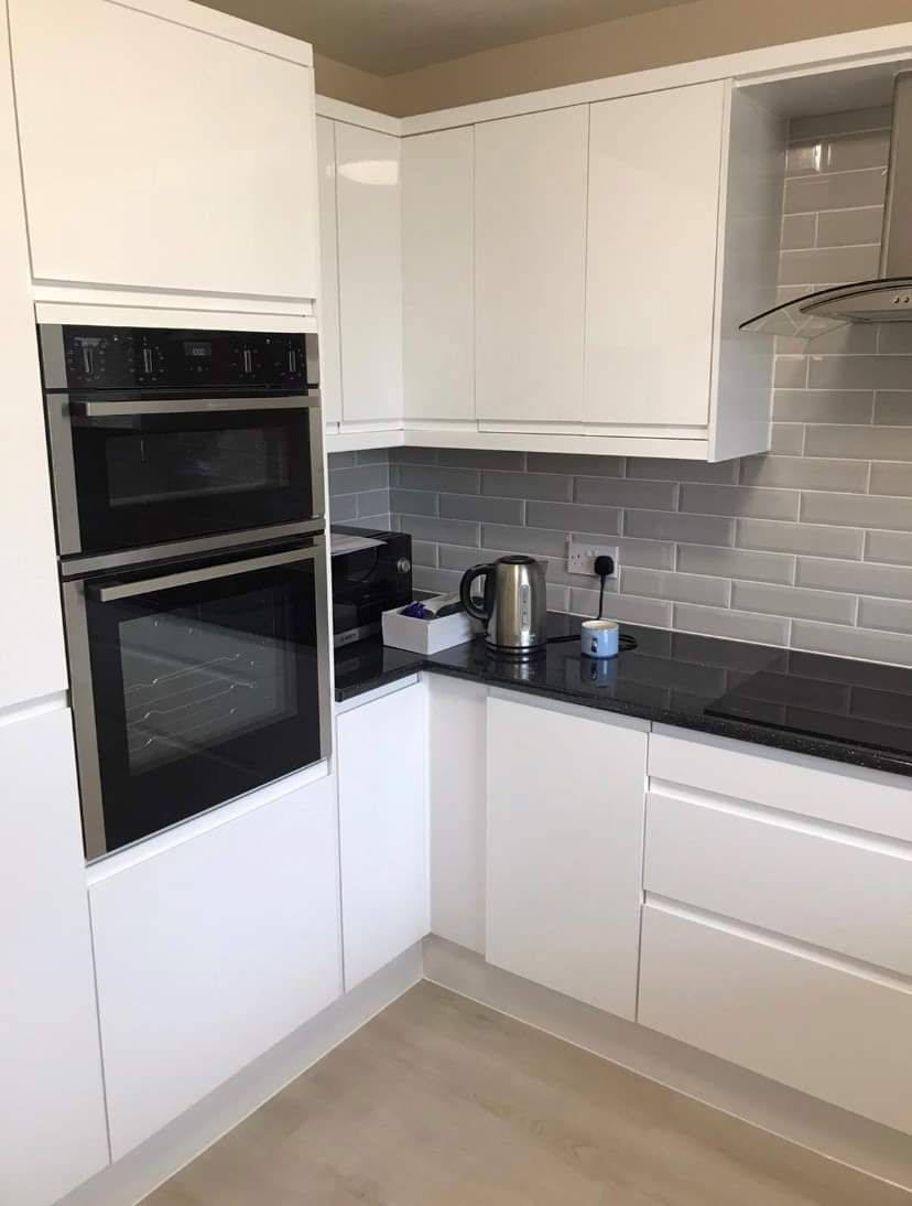 A kitchen with white cabinets , black counter tops , stainless steel appliances and a black stove top oven.