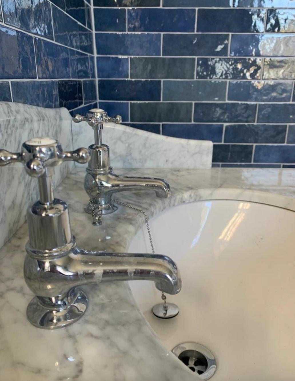 A bathroom sink with two chrome faucets and blue tiles