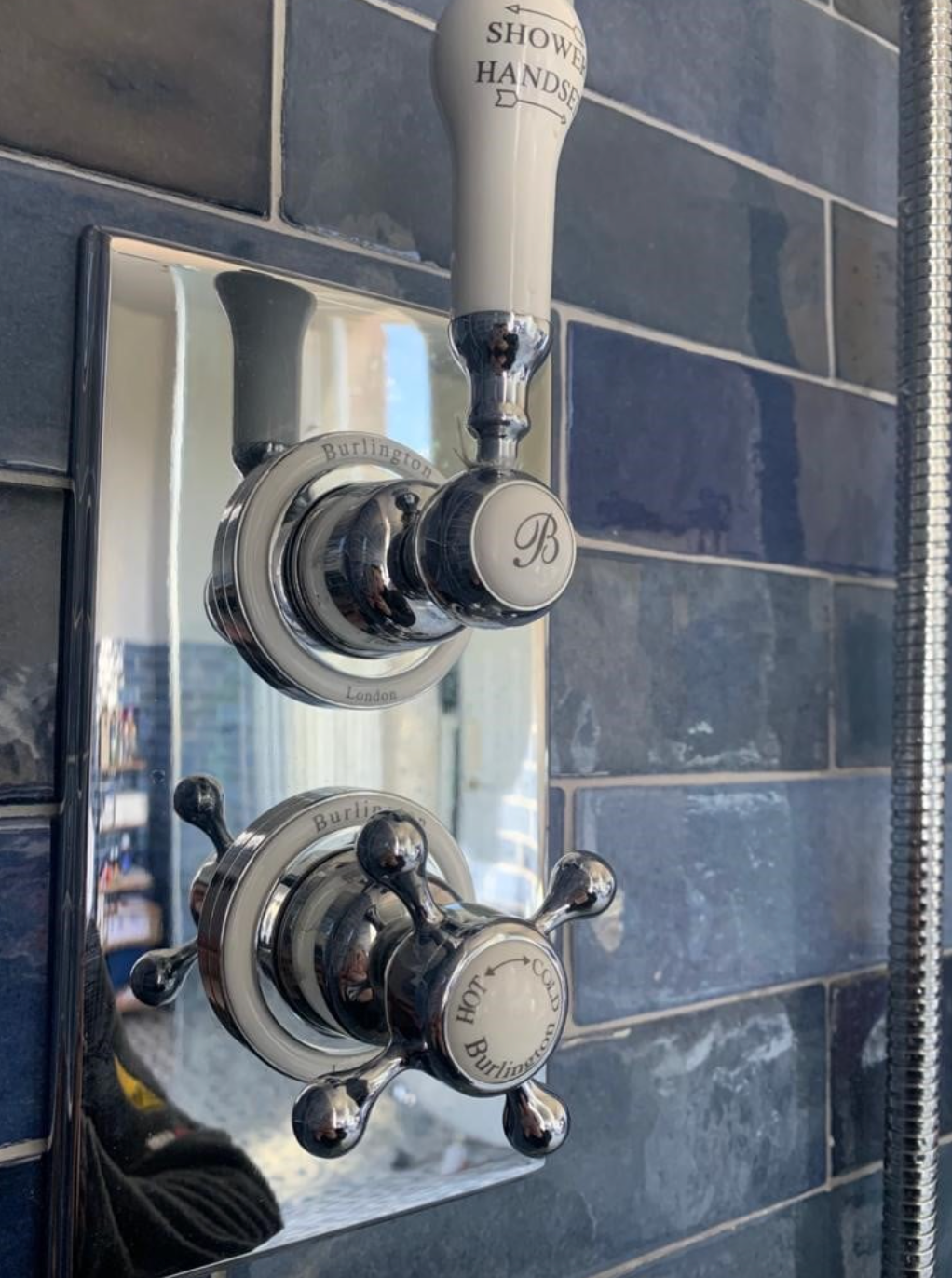 A close up of a shower faucet on a blue tiled wall.