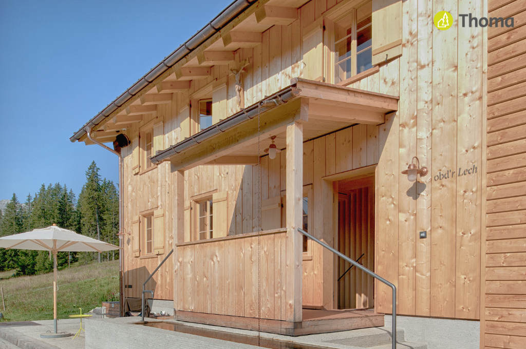 Ein Holzhaus mit Veranda und Treppe und einem Sonnenschirm davor.