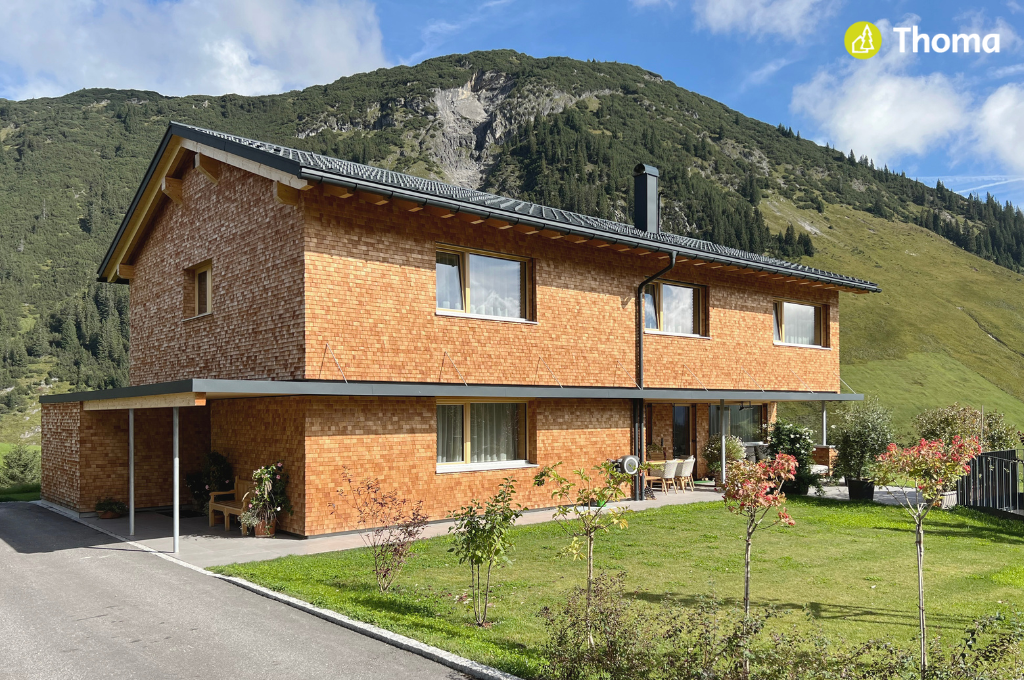 Auf einem üppig grünen Hügel steht ein Haus mit vielen Fenstern.