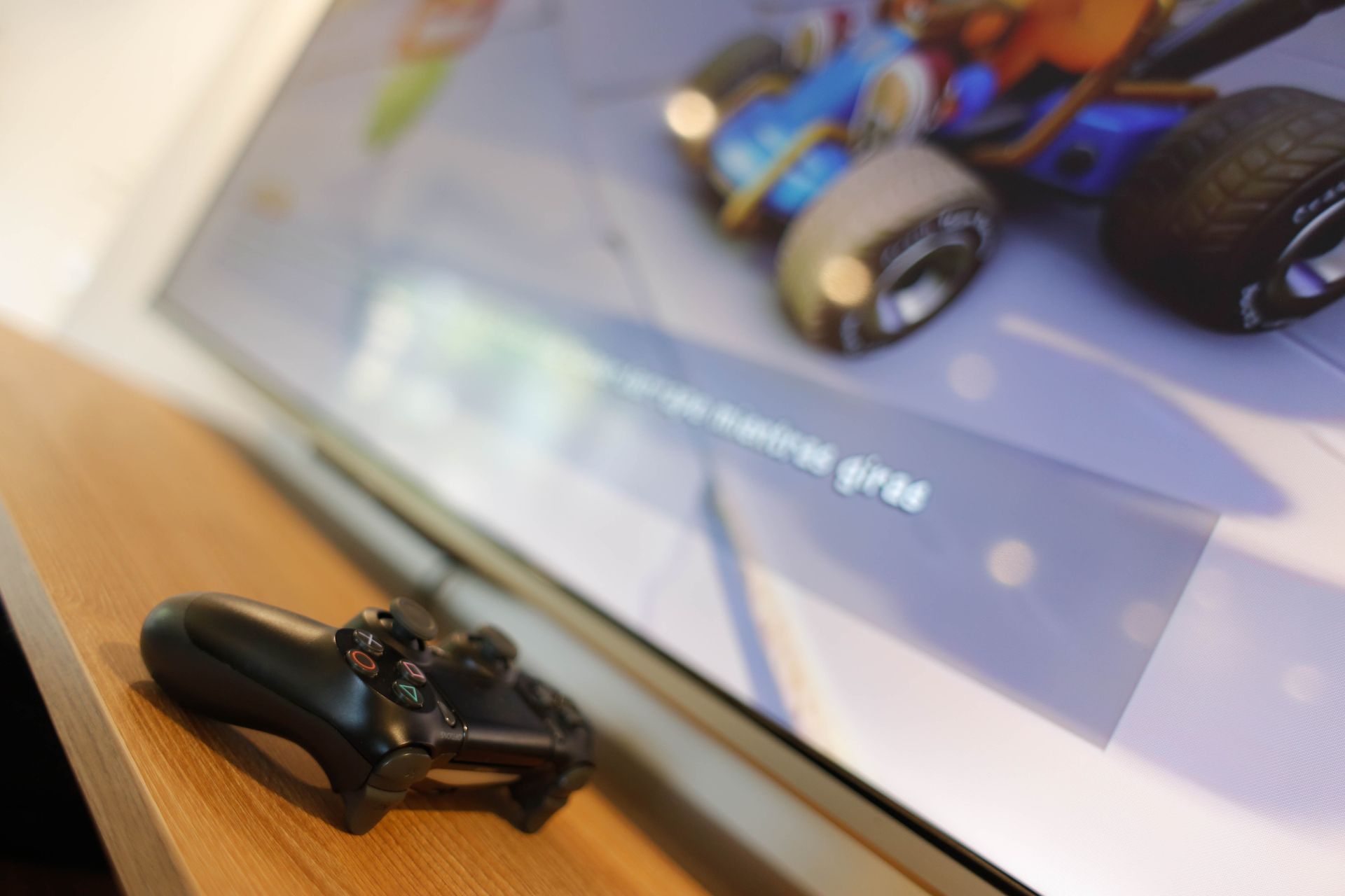 Un controlador de videojuego está sentado sobre una mesa de madera frente a un televisor.