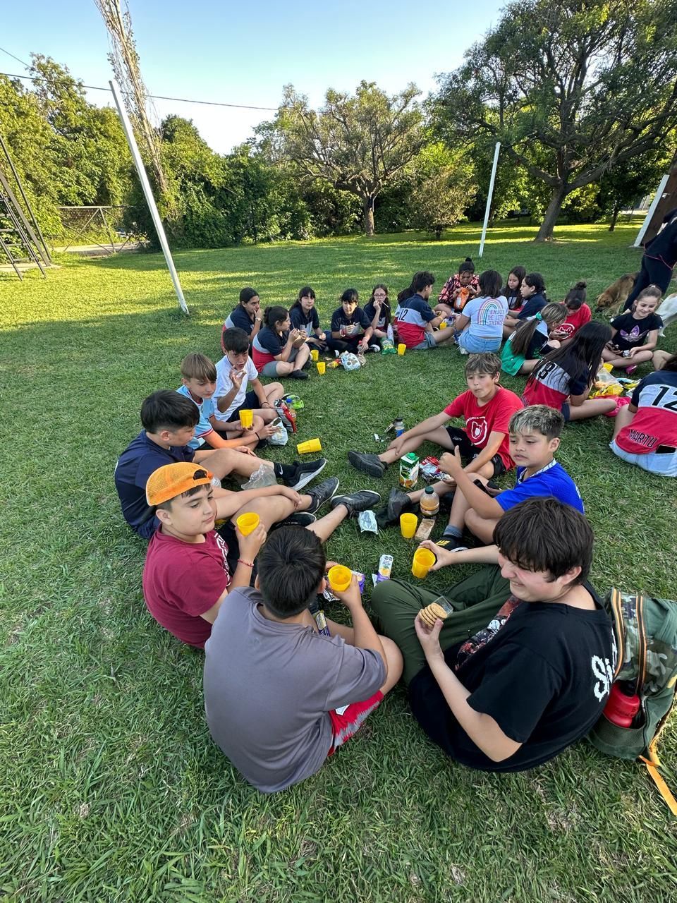 Un grupo de niños está sentado en círculo sobre el césped comiendo.