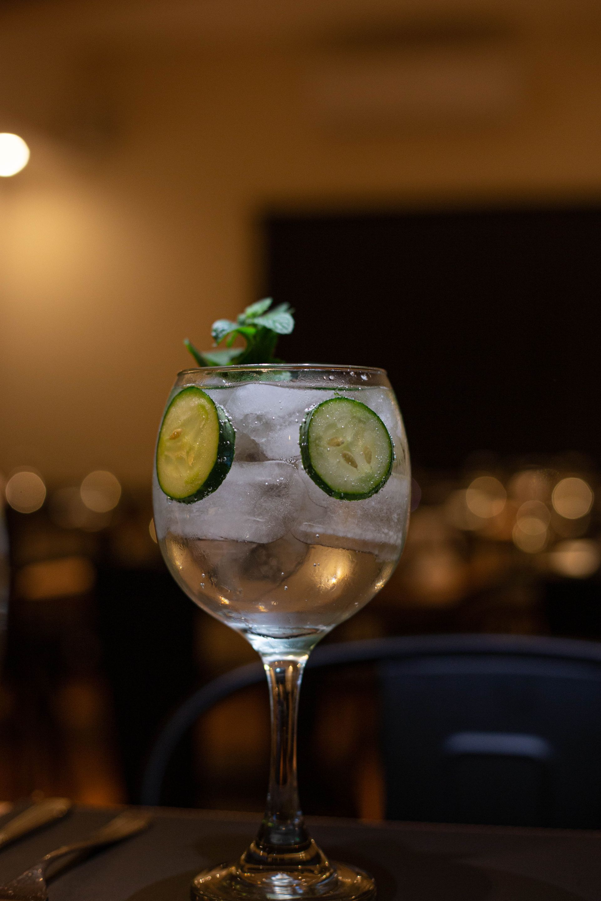 Un vaso de gin tonic con rodajas de pepino sobre una mesa.