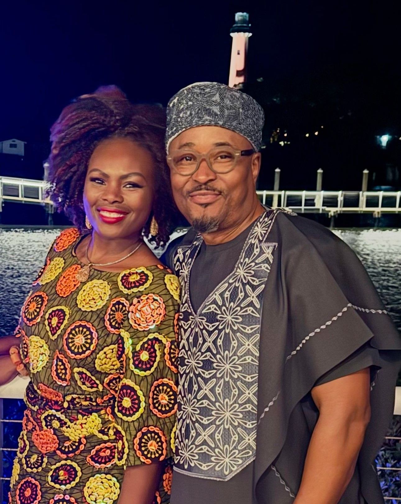 A man and a woman are posing for a picture with a lighthouse in the background