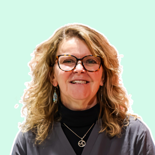 A woman wearing glasses and a necklace is smiling for the camera.