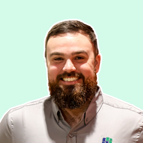 A man with a beard is smiling and wearing a grey shirt.