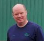 A man in a blue shirt is standing in front of a green wall.