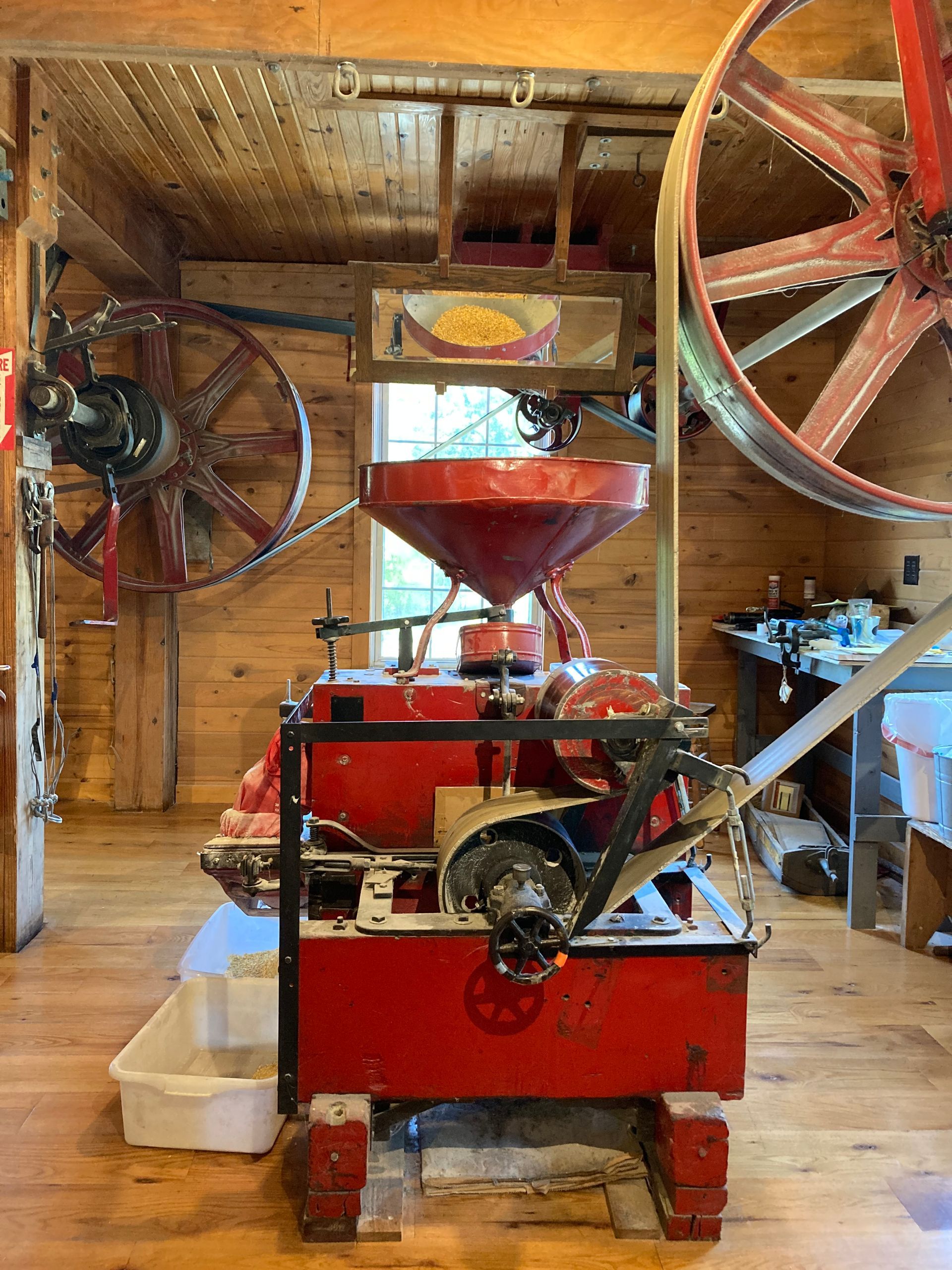 A red machine is sitting in a wooden room next to a wagon wheel.