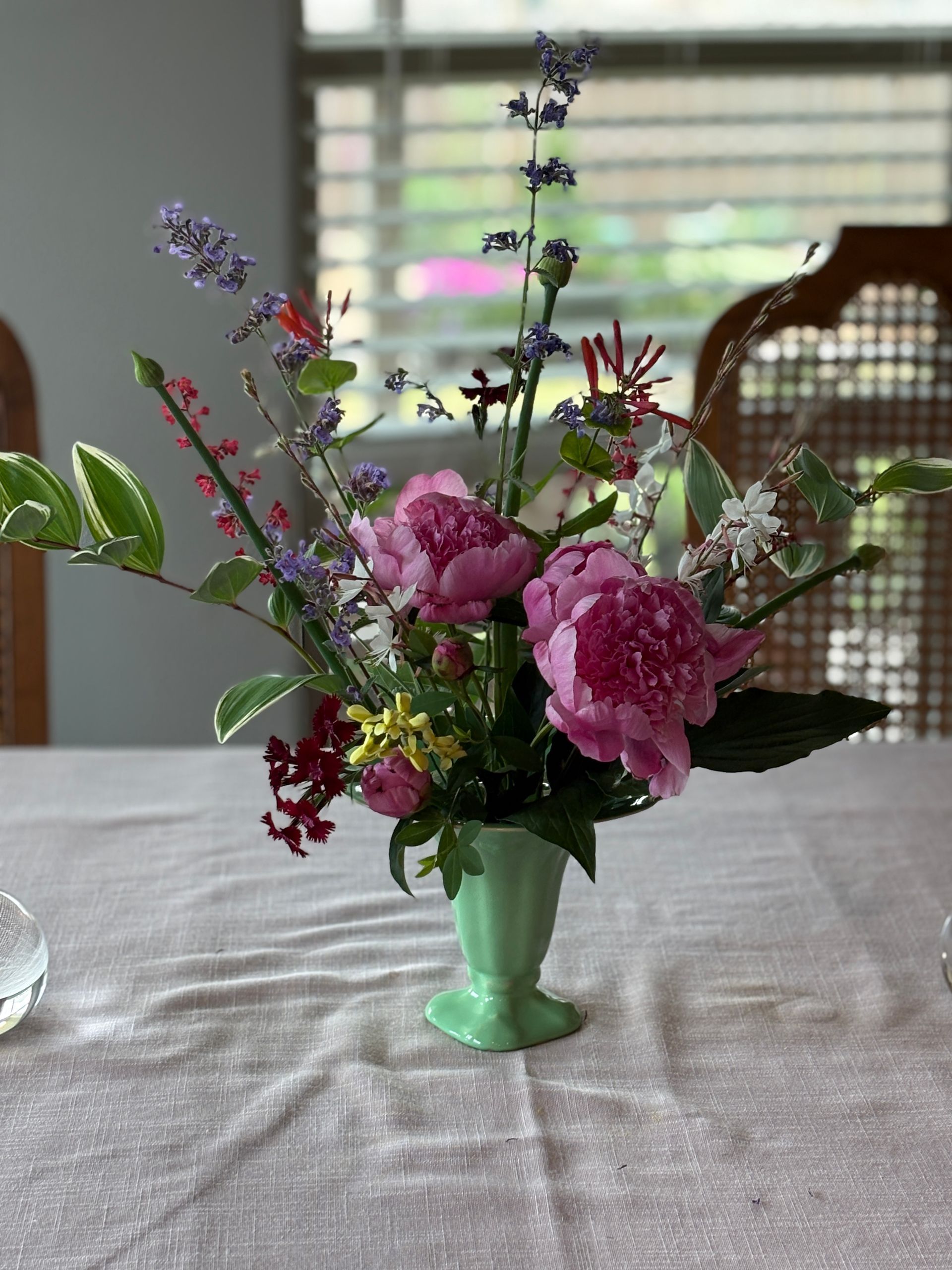 A green vase filled with flowers is sitting on a table.