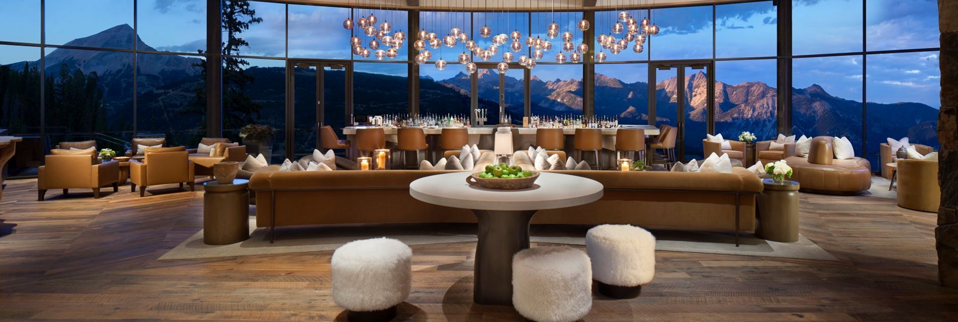 Modern hotel lounge with panoramic mountain view, warm lighting, and round dining tables by tall windows
