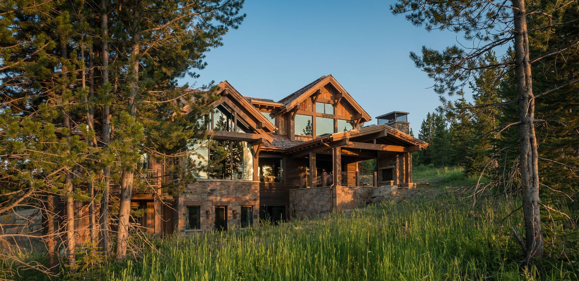 Rustic log cabin in a forest clearing at sunset, surrounded by tall trees and grass