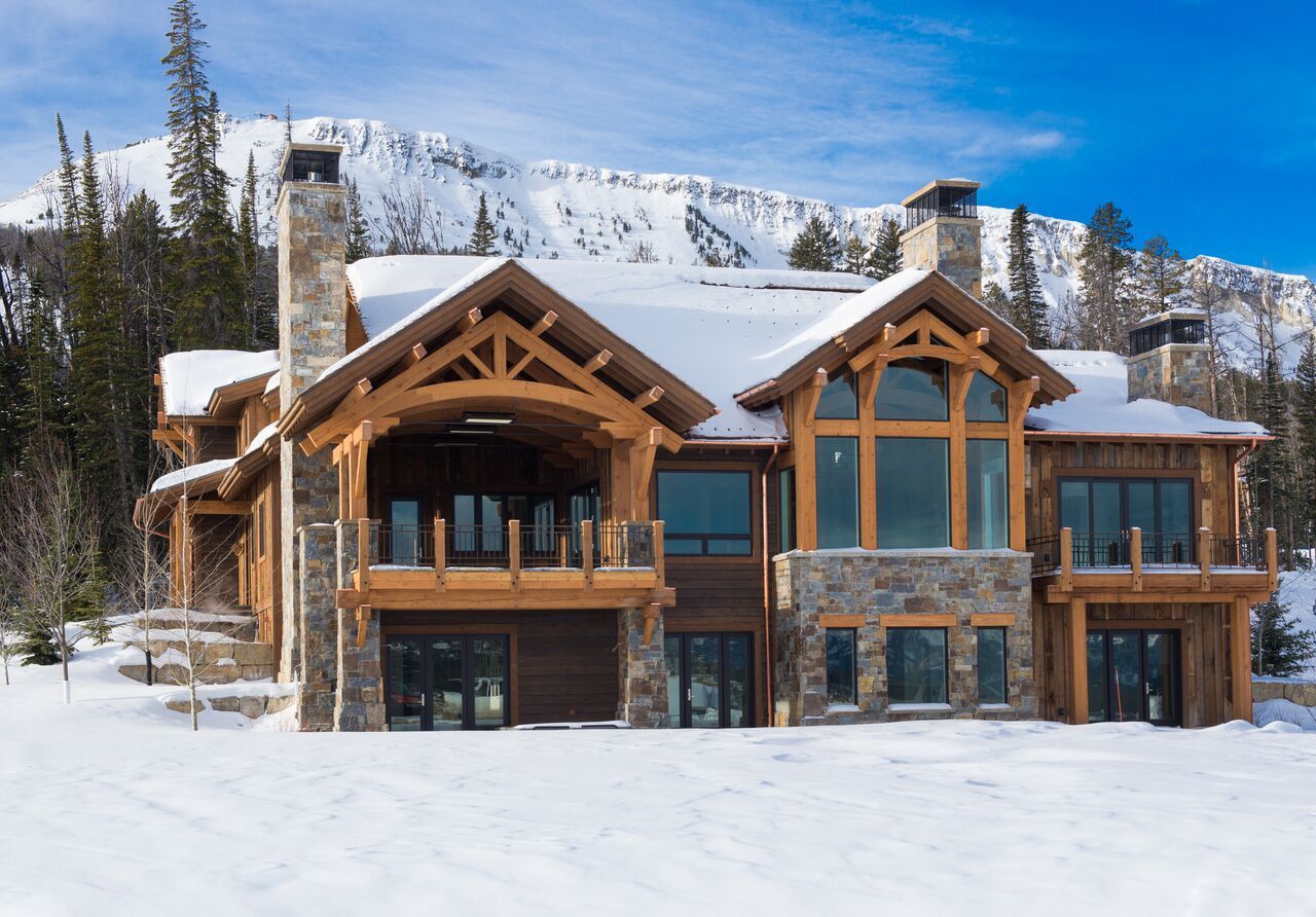 Snow-covered wooden mountain chalet with large windows and balconies under a blue sky.