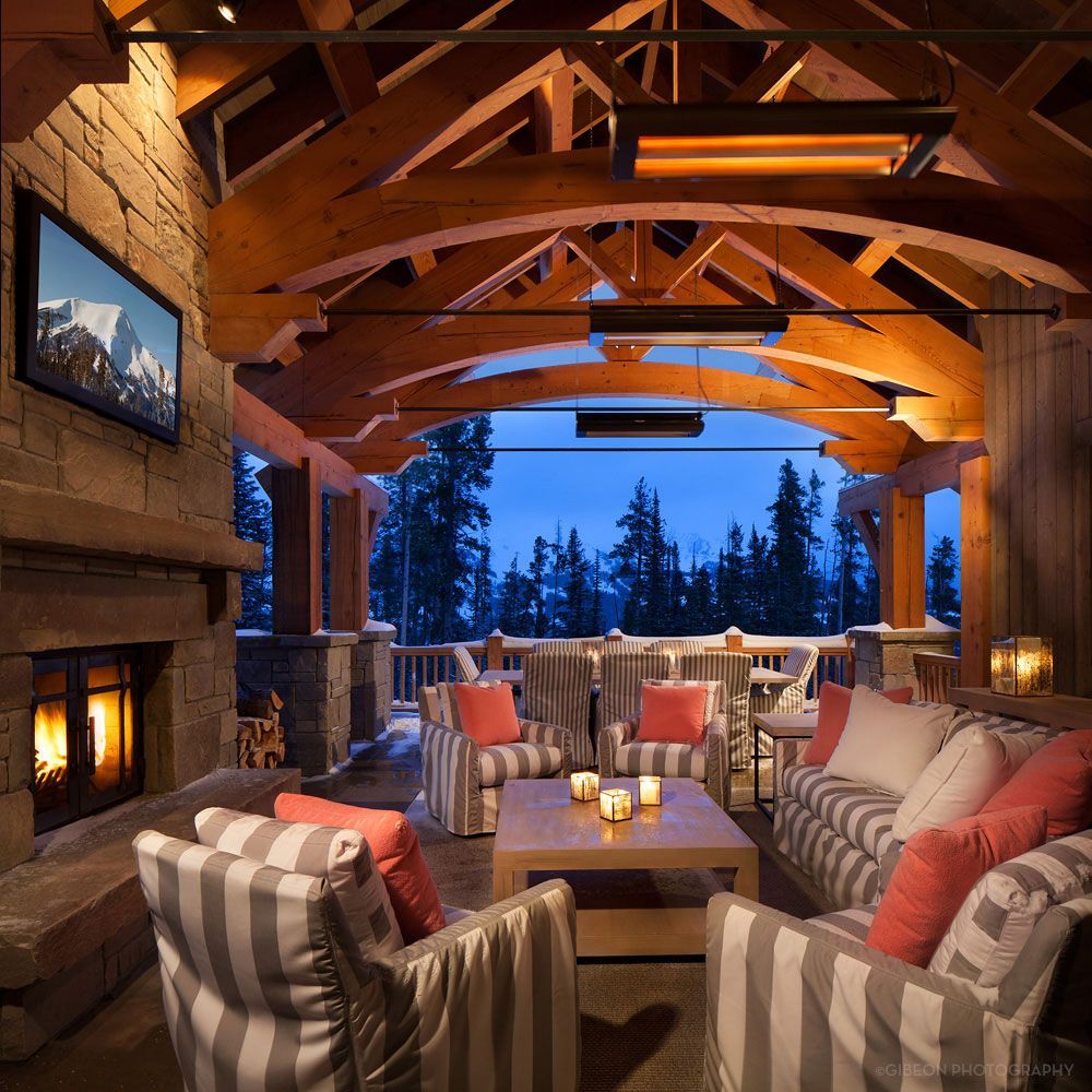 Cozy mountain lodge lounge with stone fireplace, striped chairs, and a snowy forest view through large windows