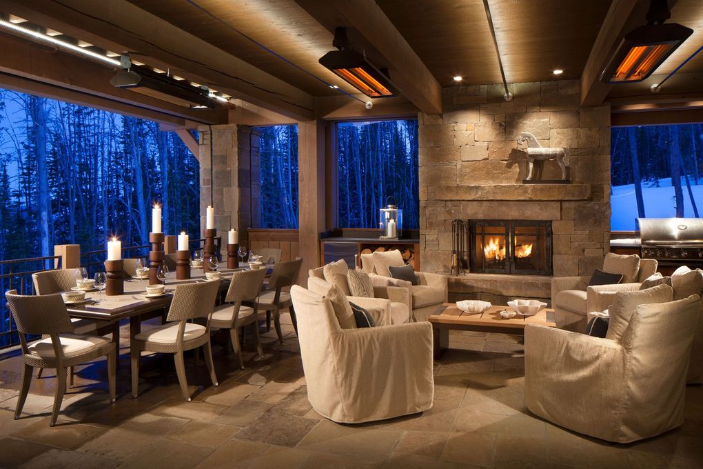 Warm, wood-paneled lounge with white sofas, dining tables, a stone fireplace, and blue forest views through large windows
