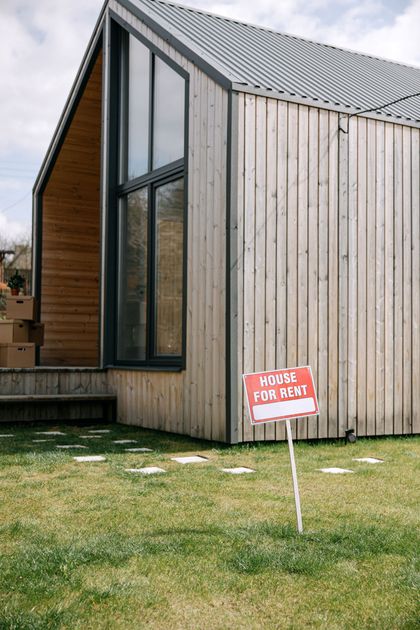 Modern wooden house exterior with tall windows and a small red sign on the lawn
