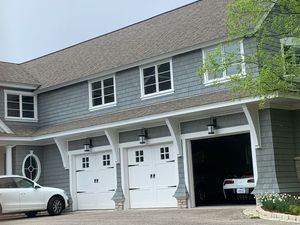 A white car is parked in front of a large house with three garage doors.