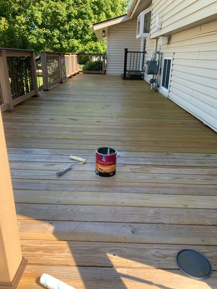 A can of paint is sitting on a wooden deck next to a house.