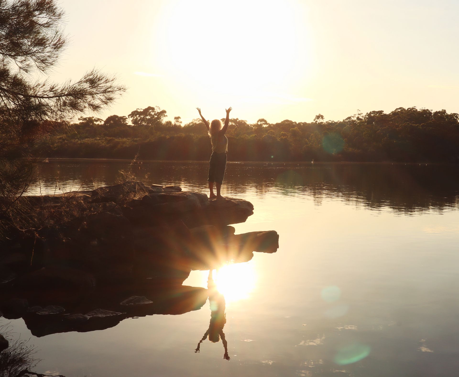 woman standing by the water with the sun and reflection