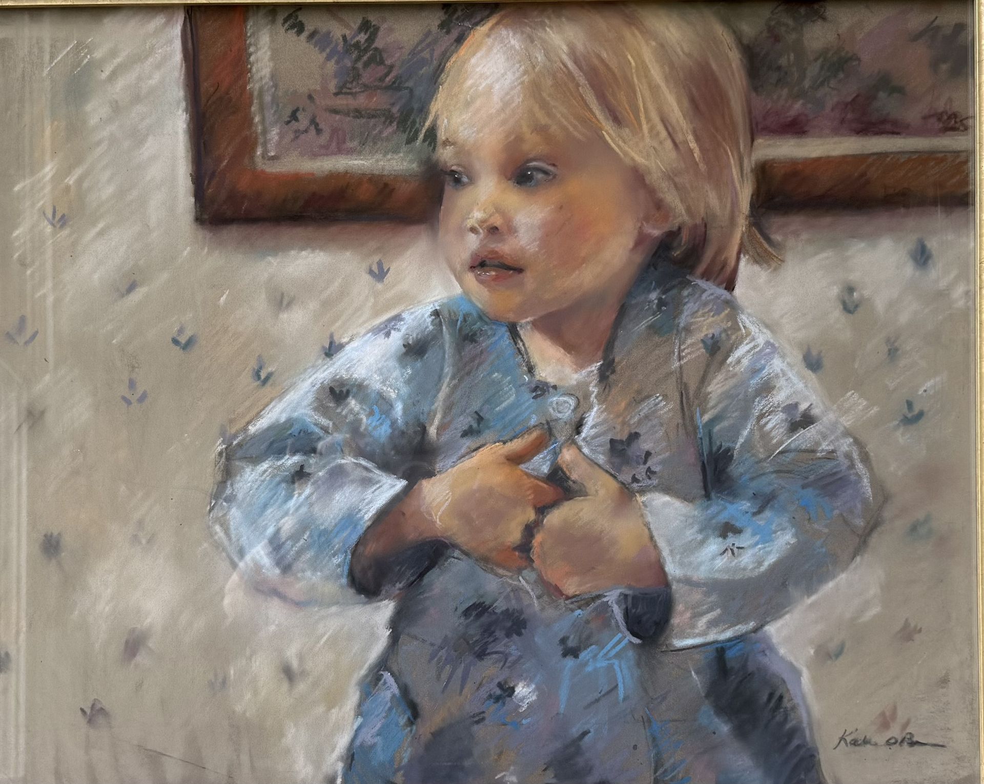 Blond toddler in a blue patterned robe, hands clasped, looking to the side. Painting hangs on the wall behind.