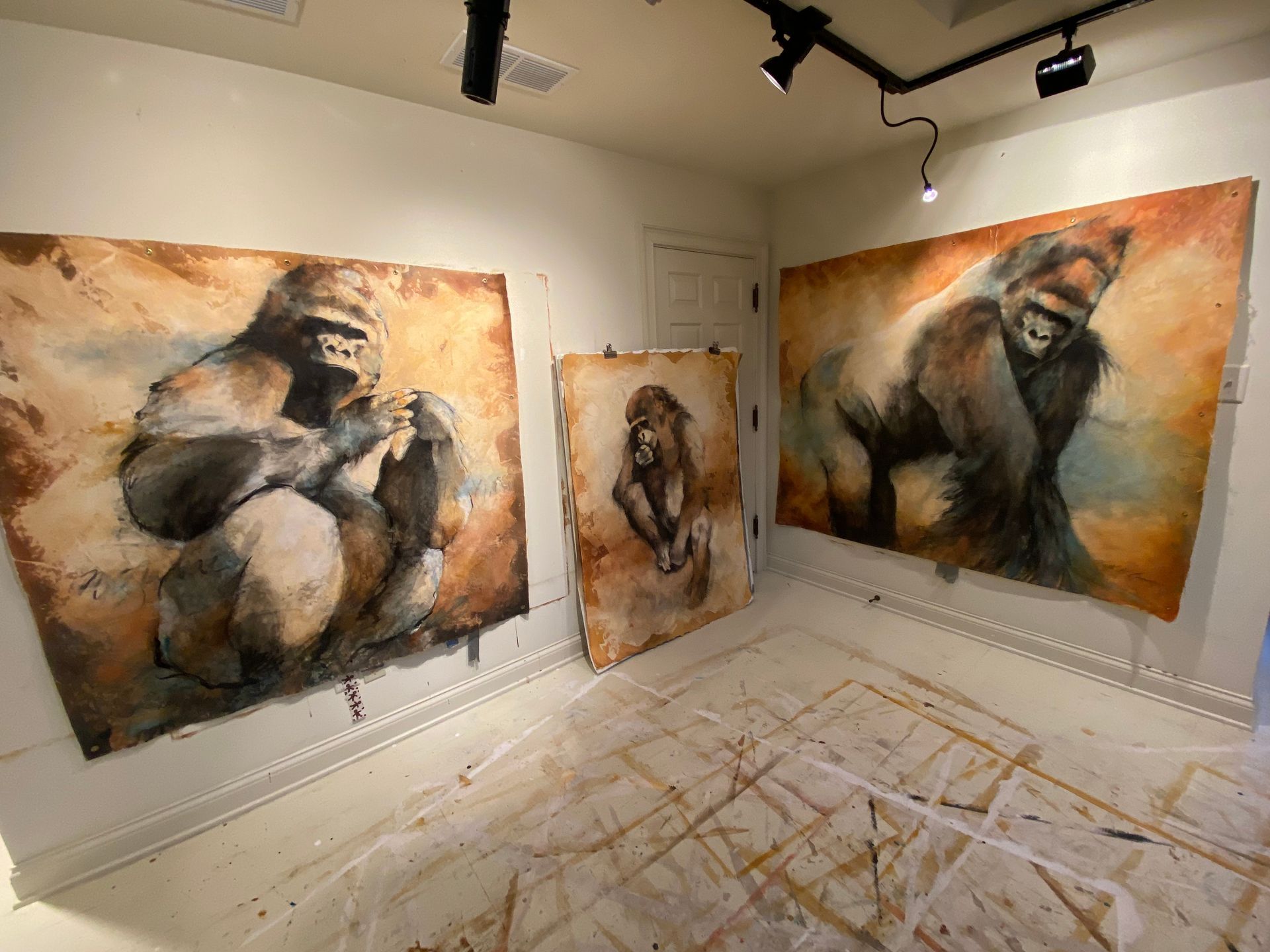 Three gorilla paintings in a room. Brown and white tones. One gorilla sits, another stands.