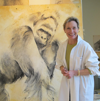 Katie O'Brien in white coat smiles, standing next to large charcoal drawing of a gorilla.
