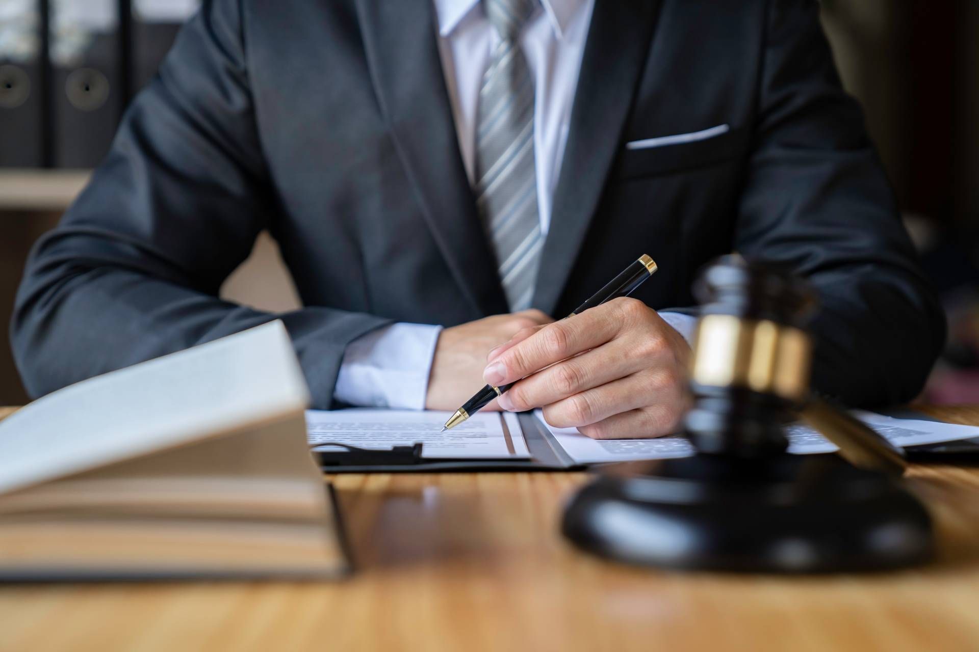 Lawyer in suit writing on a document at a desk next to a gavel and book.