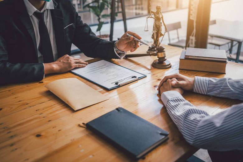 Lawyer pointing at document with client at a wooden table in office setting.
