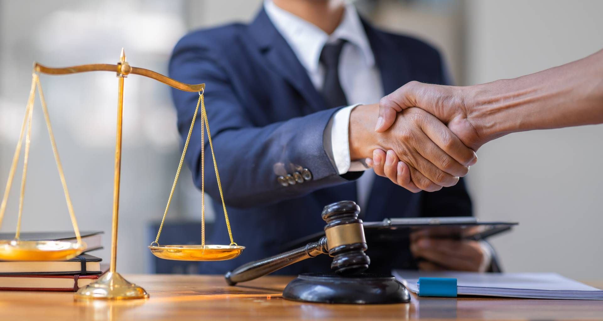 Lawyer shaking hands with a client near scales of justice and gavel on a desk.
