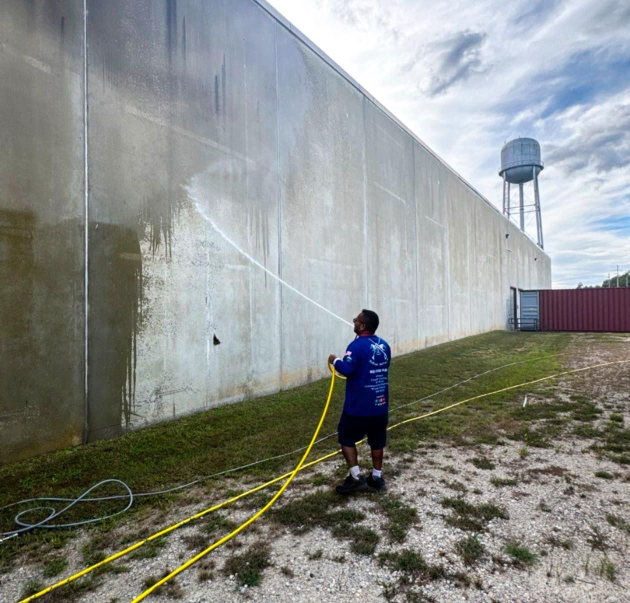 A man is using a high pressure washer to clean a pole.