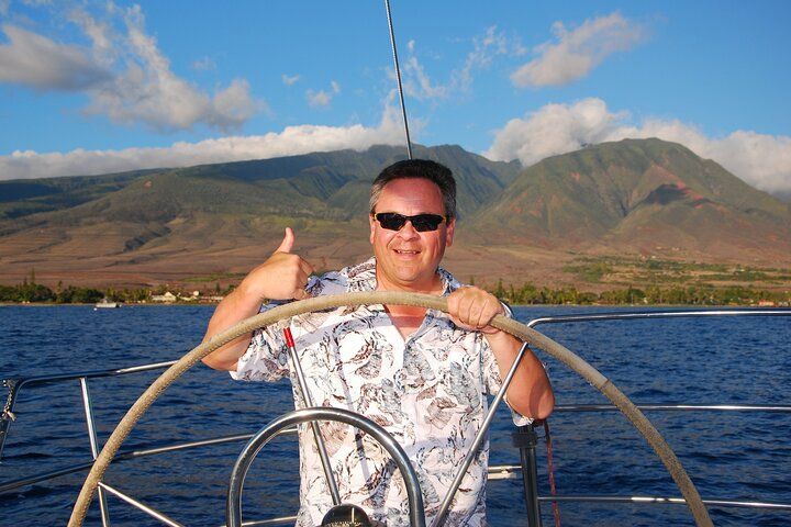 A man is giving a thumbs up while holding the steering wheel of a boat