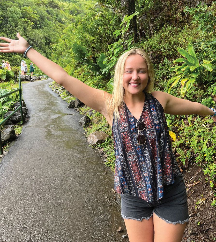 A woman is standing on a path with her arms outstretched.