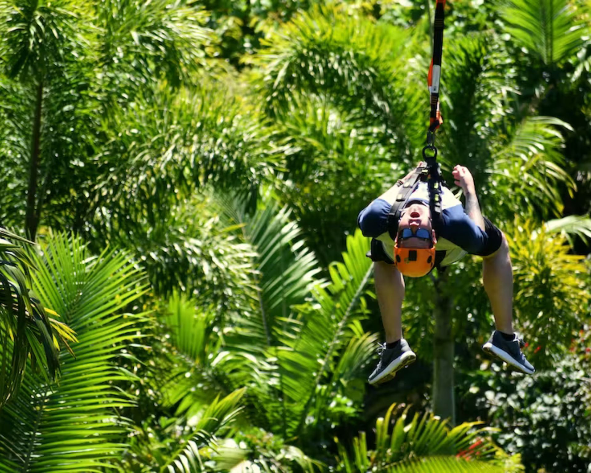 A man is flying through the air on a zip line in the jungle.
