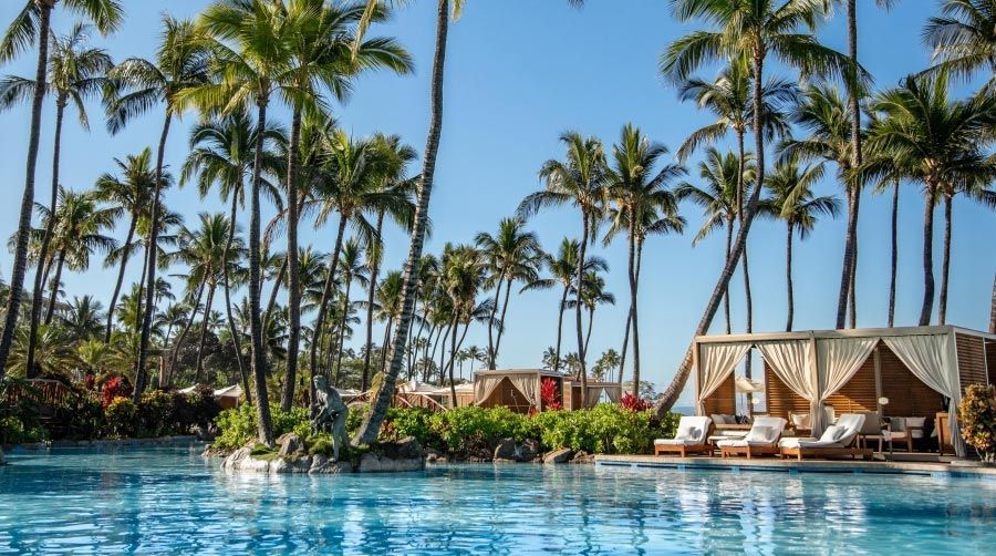 A large swimming pool surrounded by palm trees at a resort.