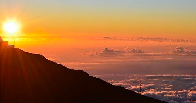 A sunset over a mountain with the sun shining through the clouds.