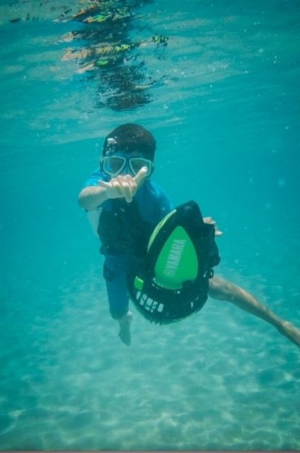 A young boy is swimming underwater with a paddle board.