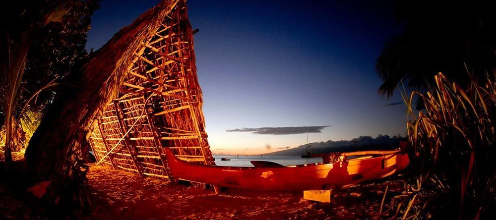 A boat is parked in front of a hut on a beach at night.