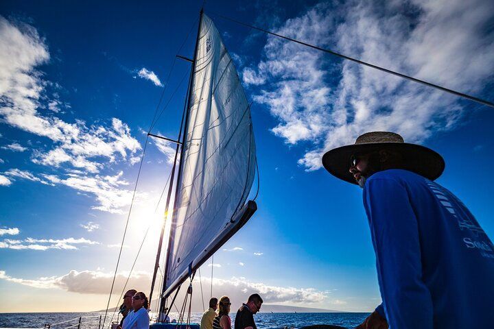 A man in a hat is standing on a sailboat in the ocean.
