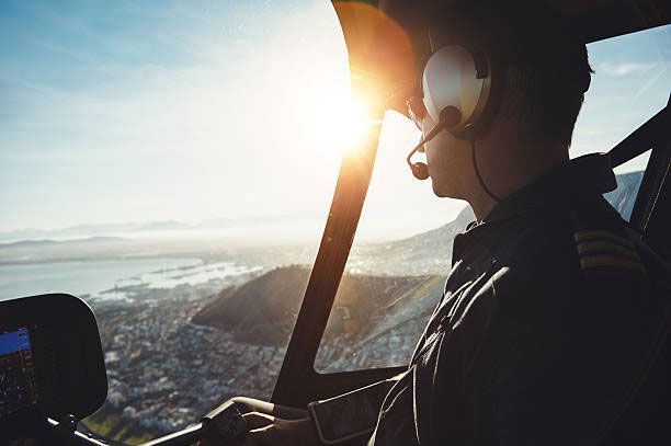 A pilot wearing headphones is flying a helicopter over a city.