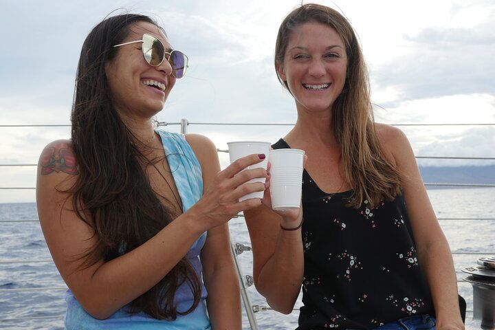 Two women are toasting with cups on a boat in the ocean.