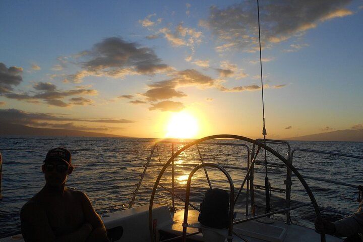 A person is sitting on a boat in the ocean at sunset.